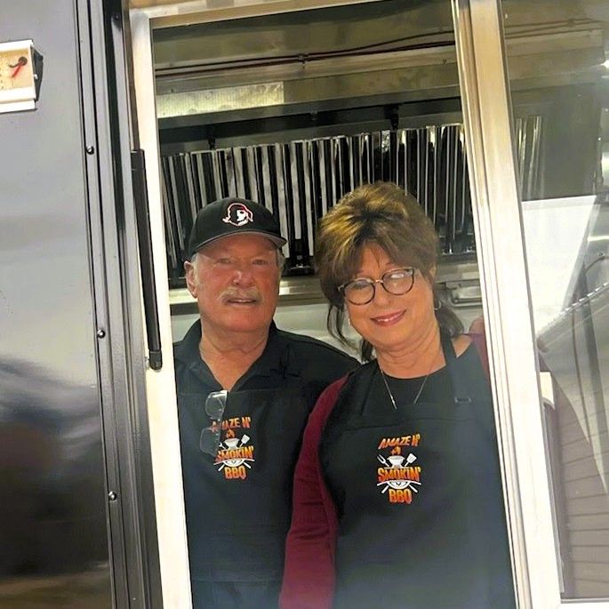 Friendly couple at the window of the Amaze N' Smokin' BBQ trailer.