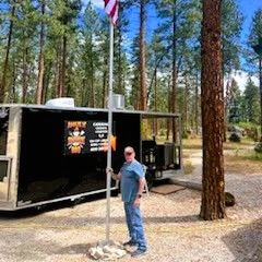 Man standing beside a flagpole near the Amaze N' Smokin' BBQ trailer.