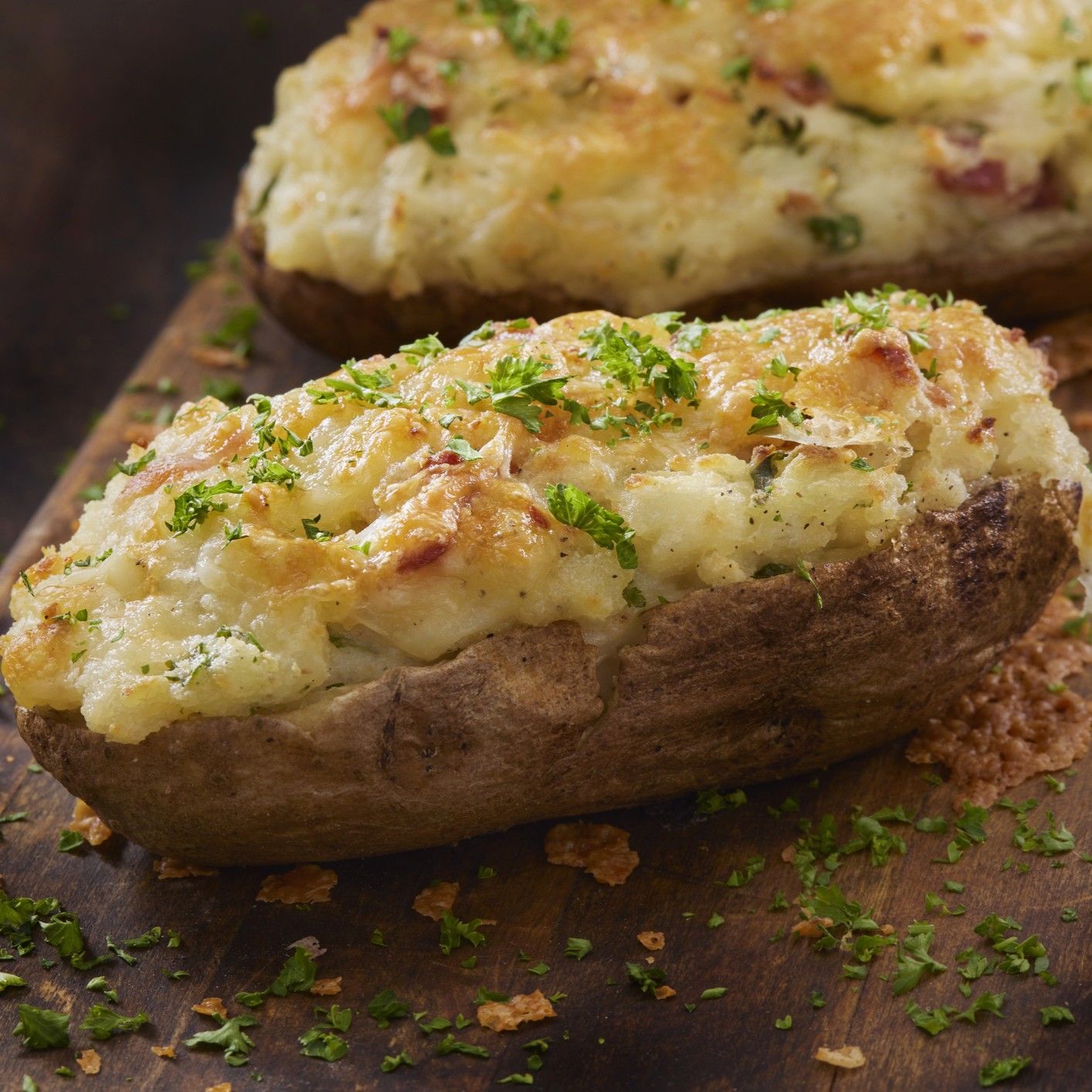 Twice backed potatoes with cheese and chives on a wood cutting board.